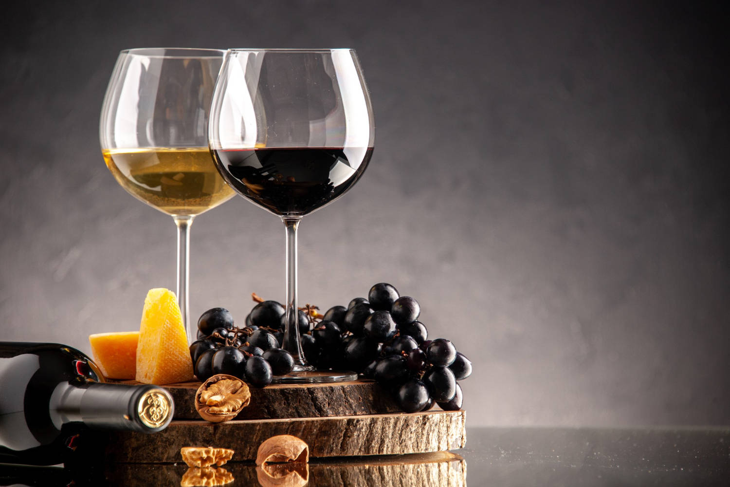 front-view-wine-glasses-fresh-grapes-walnuts-yellow-cheese-wood-board-overturned-bottle-dark-background